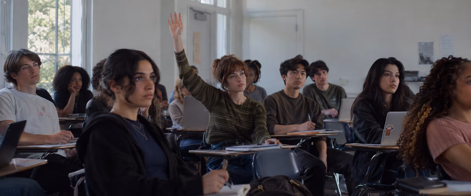 Students in a classroom listening while one student raises a hand