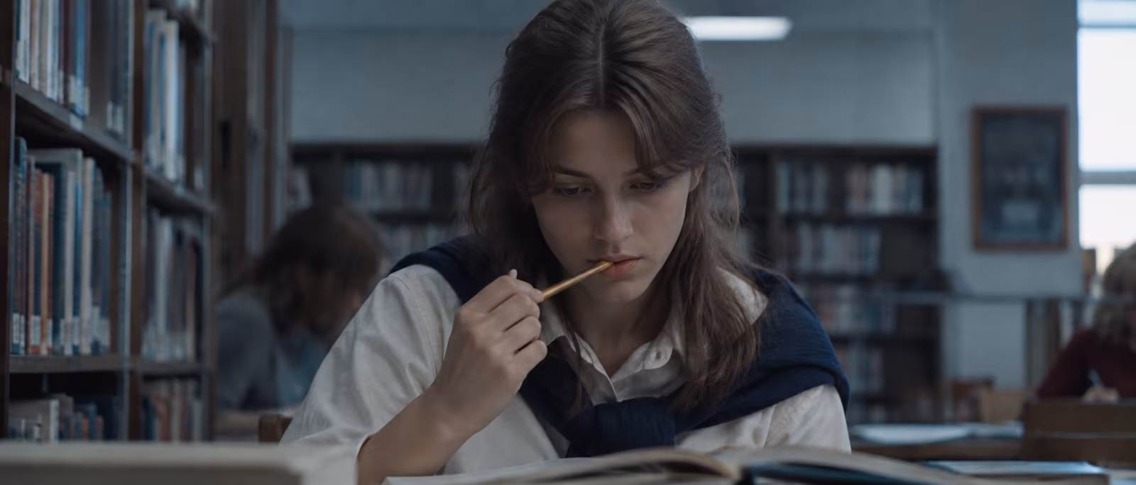 A student reading in a library with a pencil and an open book