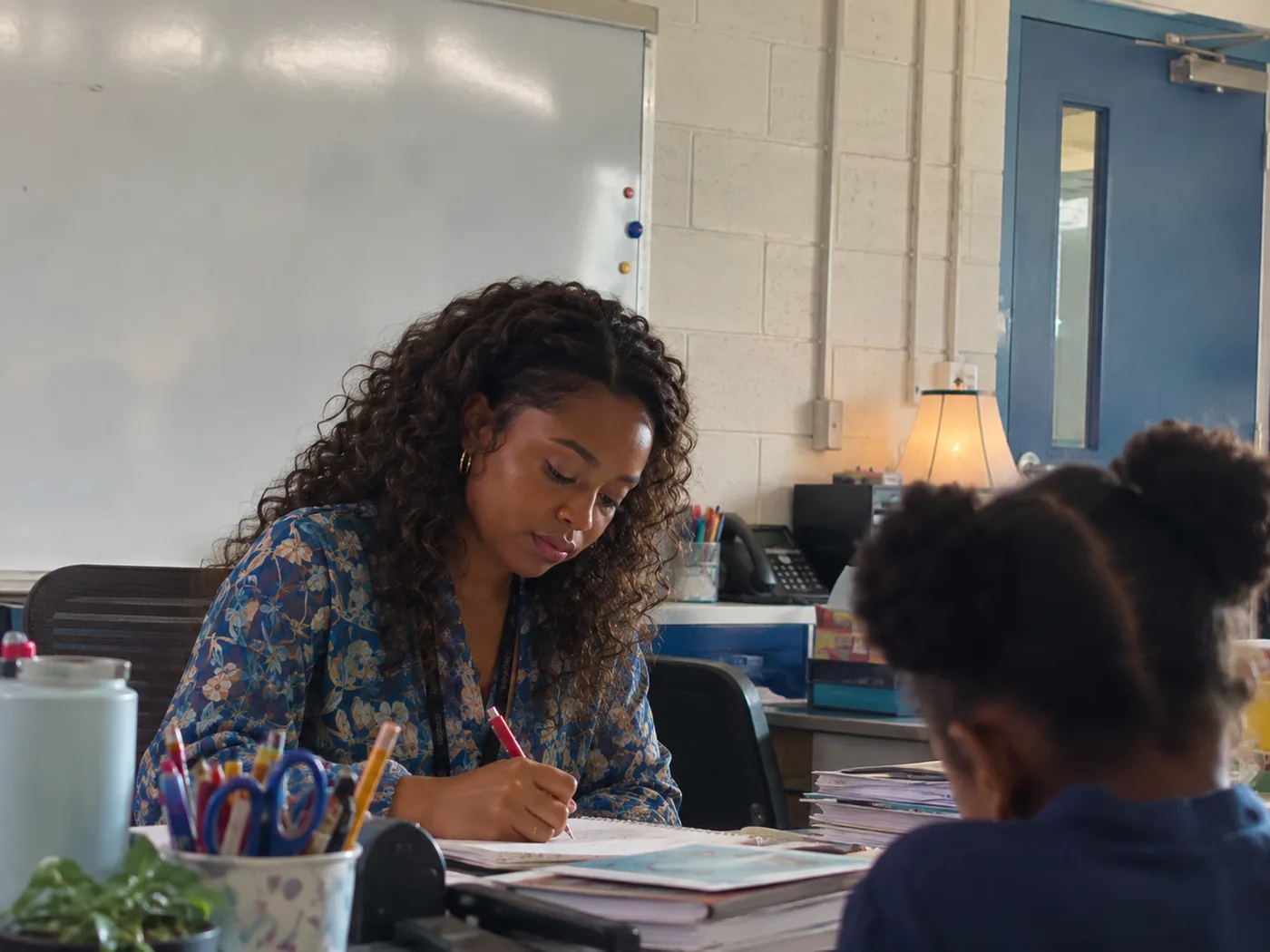 Adult learner writing notes at a desk while another student studies nearby.